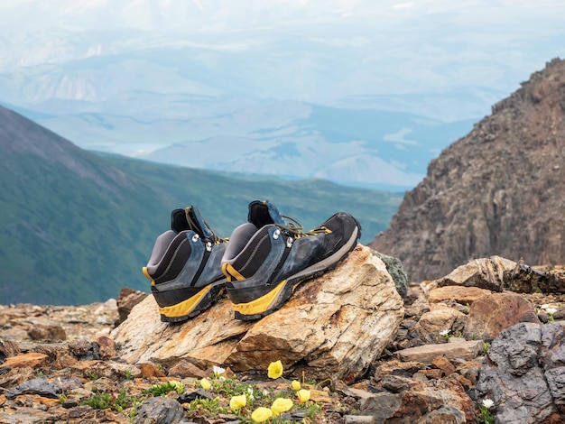 Des chaussures de randonnée mouillées sèchent sur une pierre sur fond de hautes montagnes enneigées Les difficultés de la randonnée à sécher les vêtements dans la nature