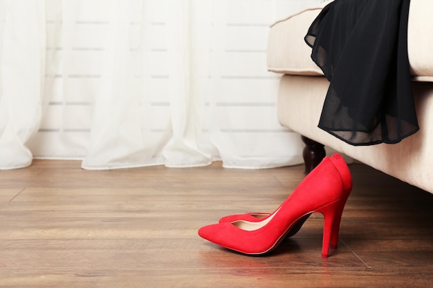 Chaussures rouges sur parquet près de canapé avec robe noire dans la chambre