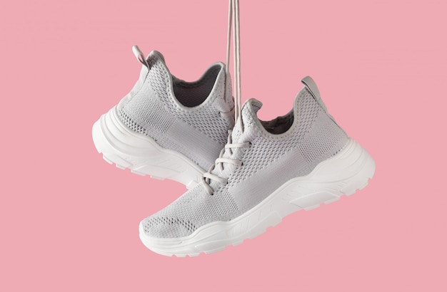 Photo chaussures de sport féminines élégantes de mode pour courir accrocher sur fond rose. baskets grises en textile à semelles blanches. gros plan avec copie espace