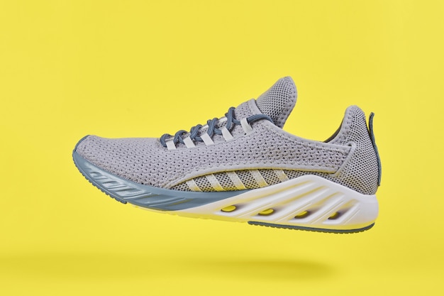 Chaussures de sport grises pour courir sur un mur jaune. Concept de mode de vie sain, de sport et de remise en forme. Couleur 2021 année. Baskets à coussin de mode.