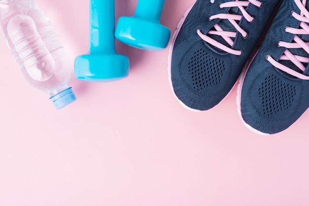Chaussures de sport pour femmes, haltères bleus et bouteille d'eau sur fond rose