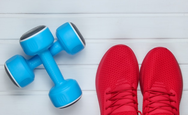 Chaussures de sport rouges pour l'entraînement, haltères sur plancher en bois blanc. Vue de dessus.