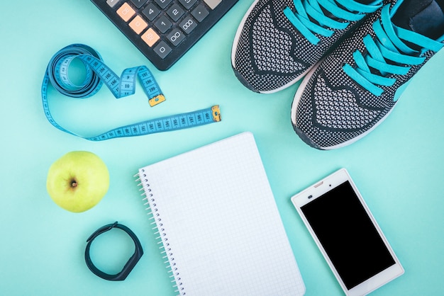 Chaussures de sport, smartphone, ruban adhésif, calculatrice, bracelet de remise en forme et pomme verte sur fond vert ou bleu