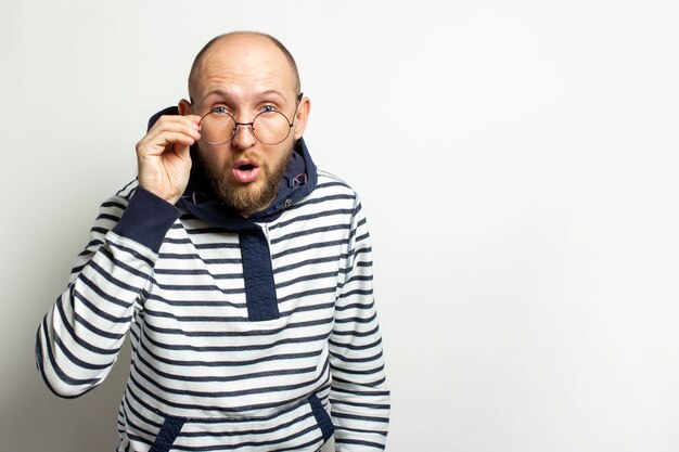 Chauve Jeune homme à la barbe, un pull à capuche baissa ses lunettes sur son nez avec un visage surpris sur un blanc isolé. Espace copie