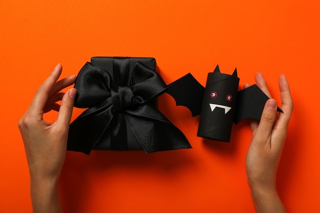 Chauve-souris en papier cadeau et mains sur fond orange, vue de dessus