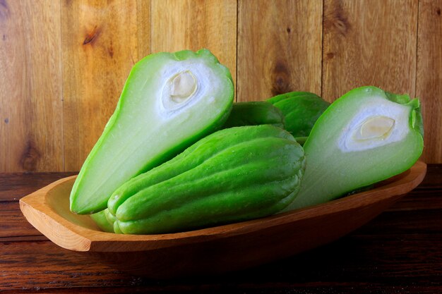 Chayote crue, fraîche et biologique, entière et tranchée dans un panier sur une table en bois rustique