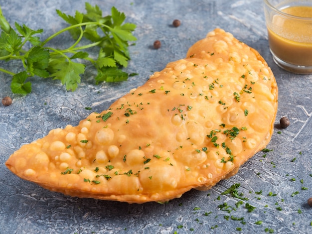 Cheburek savoureux avec de la viande et de la vinaigrette à la moutarde décorée de légumes verts sur fond gris