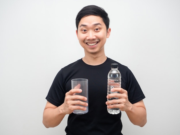 Cheefull homme asiatique tenant une bouteille d'eau et un verre à la main sur fond blanc