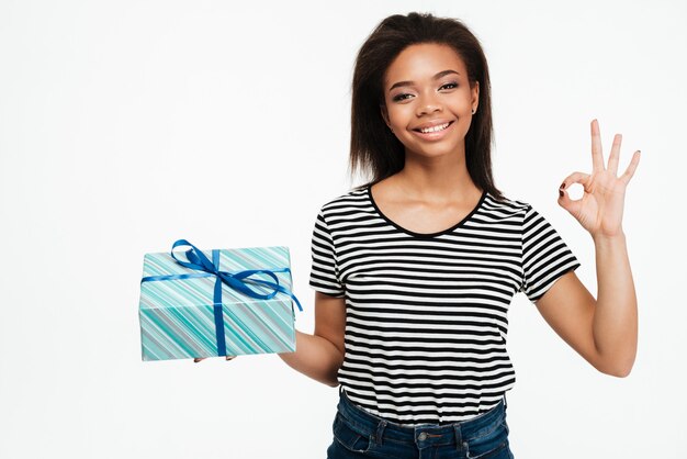 Cheerful african woman holding coffret cadeau et montrant le geste ok