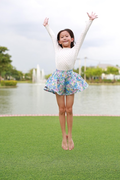 Cheerful Asian young girl kid sautant dans le jardin en plein air