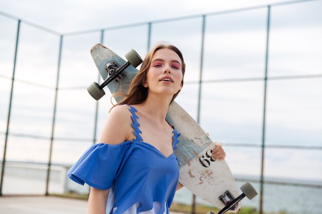 Cheerful attractive young woman holding skateboard debout à l'extérieur