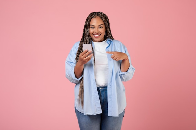 Cheerful Black Plump Lady à l'aide de téléphone debout sur fond rose