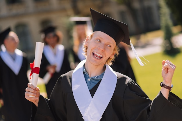 Cheerful boy célébrant sa réception d'un diplôme de maîtrise dans la cour de l'université