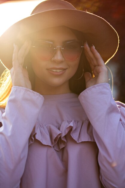 Cheerful brunette woman wearing hat et lunettes de soleil, posant au coucher du soleil