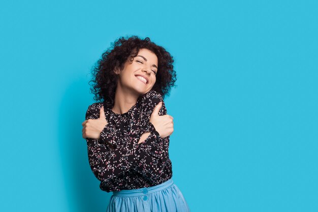 Cheerful caucasian lady aux cheveux bouclés s'embrassant sur fond bleu en souriant