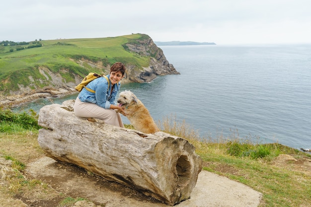 Cheerful caucasian woman hugging her dog s'asseoir sur un banc de falaise. Vue horizontale d'une femme voyageant avec un animal. Concept d'animaux et de voyage.