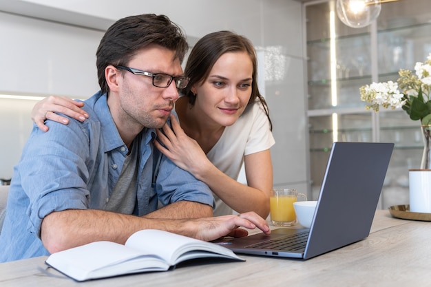 Cheerful couple looking at screen of laptop at home