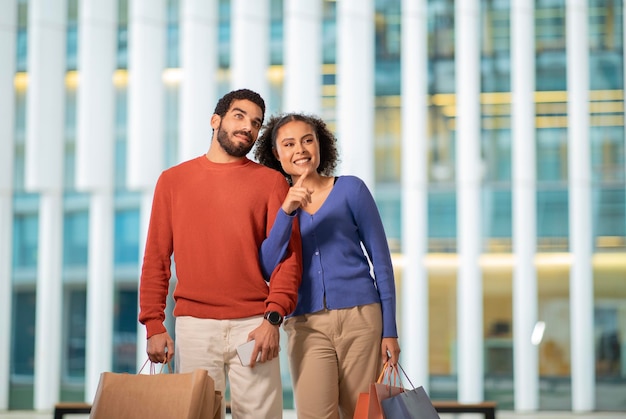 Cheerful Divers Conjoints Shopping Doigt pointé debout avec des sacs à l'extérieur