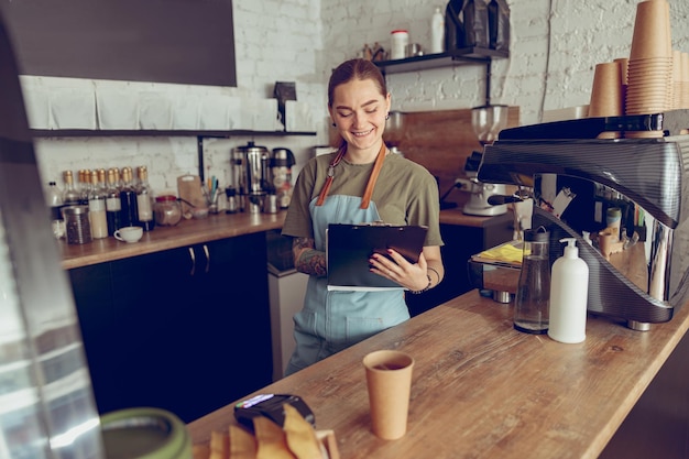 Cheerful female barista écrit sur le presse-papiers au café