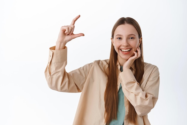 Cheerful genz girl montrant une petite chose de petite taille souriant heureux de démontrer quelque chose sur l'espace de copie montrant une petite main debout sur fond blanc