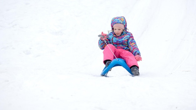 Cheerful girl riding a luge en descente sur une piste de luge couverte de neige dans un paysage de montagne d'hiver ensoleillé blanc