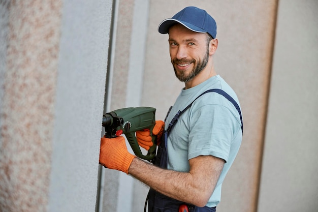 Cheerful male builder mur de forage avec perceuse électrique