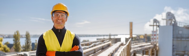 Cheerful male worker standing at industrial site against blue sky