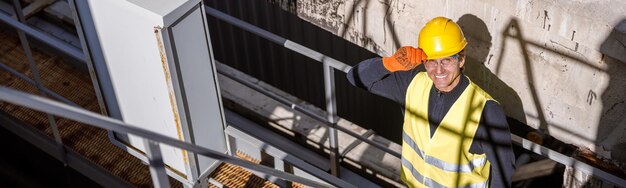 Cheerful male worker standing on metal bridge at factory