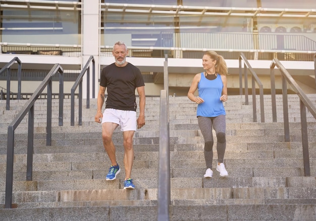 Cheerful mature couple man and woman in sportswear s'entraînant ensemble à l'extérieur dans les escaliers en ville