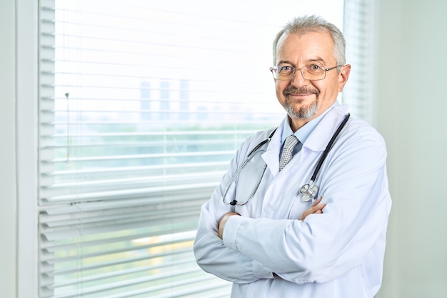 Cheerful mature doctor posant et souriant avec les bras croisés