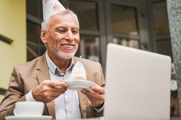 Cheerful senior man célébrant son anniversaire avec un appel vidéo à la terrasse du café