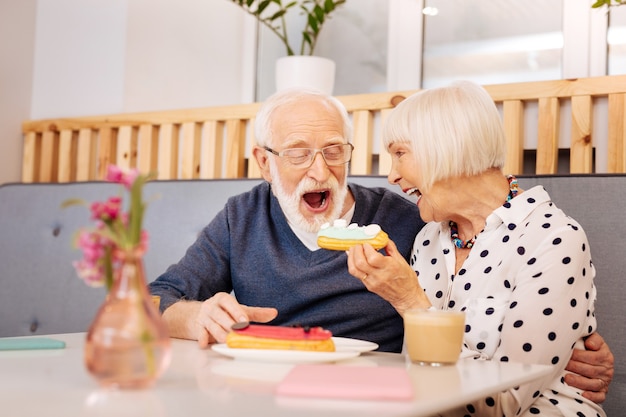 Cheerful senior woman holding eclair et senior man le manger