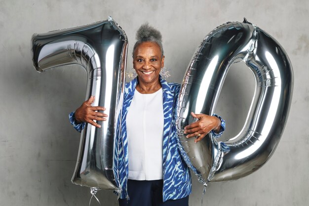 Cheerful senior woman holding silver balloons pour son 70e anniversaire