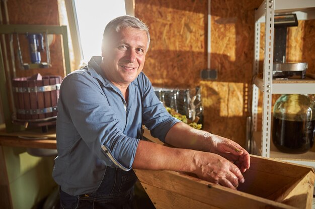 Cheerful winery worker s'appuyant sur un broyeur de raisins en se tenant debout sur son lieu de travail