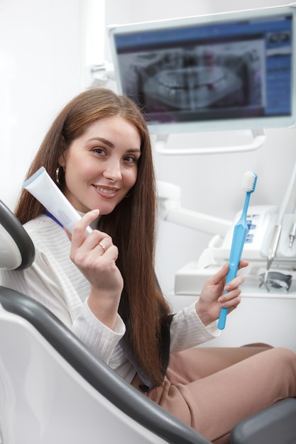 Cheerful woman holding brosse à dents et dentifrice, assis dans un fauteuil dentaire