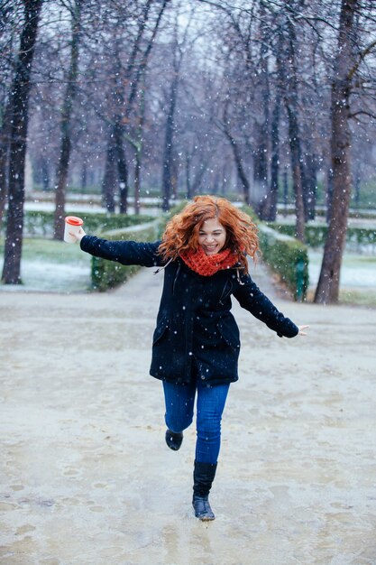 Cheerful woman jumping on flaques sous la neige dans le parc