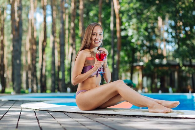 Cheerful woman se sentir soulagé et reposé tout en passant sa journée près de la piscine extérieure