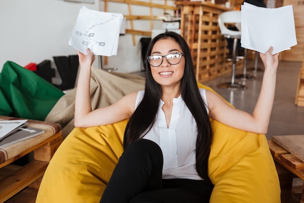 Cheerful woman sitting in bean bag chair et tenant des papiers