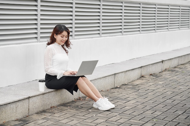 Cheerful woman using laptop assis sur les traces