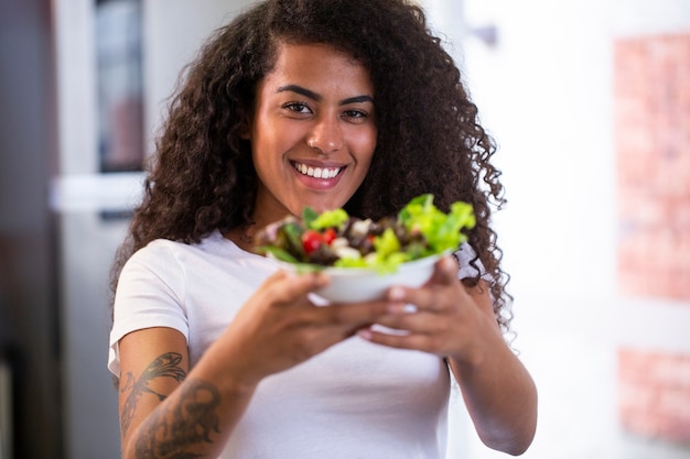 Cheerful young afro american woman eating salade de légumes dans la cuisine à domicile