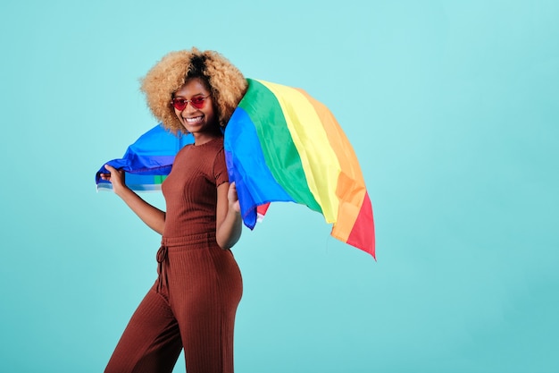 Cheerful young afro woman brandissant un drapeau de fierté sur un fond isolé. Concept de communauté LGBTQ.