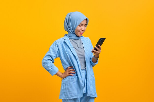 Cheerful young Asian woman looking at mobile phone isolé sur fond jaune