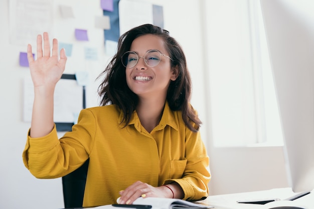 Cheerful young female office worker a levé la main pour saluer quelqu'un