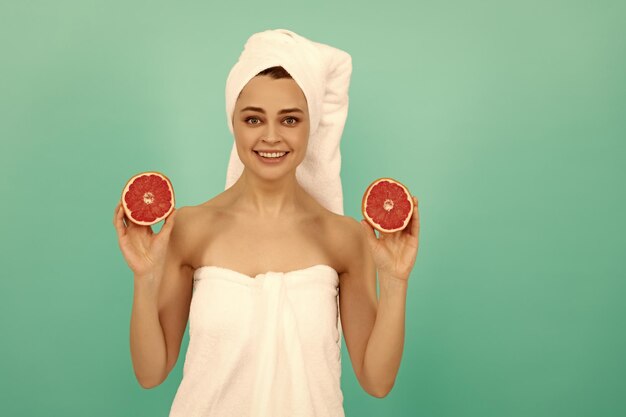 Cheerful young woman in towel après douche avec pamplemousse sur fond bleu