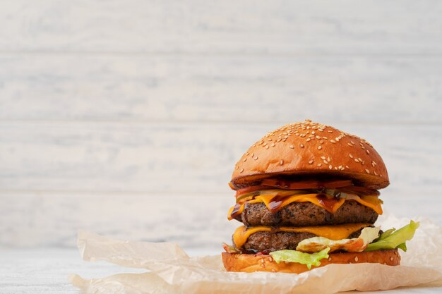 Cheeseburger double servi sur planche de bois contre un arrière-plan flou blanc