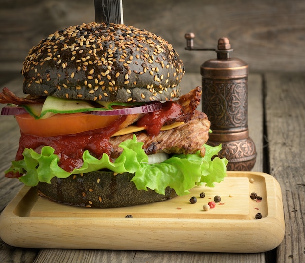 Cheeseburger avec pain noir, viande et légumes sur une surface en bois, restauration rapide