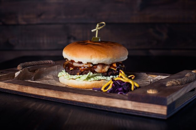 Cheeseburger sur un plateau en bois dans un restaurant, sur une surface sombre.