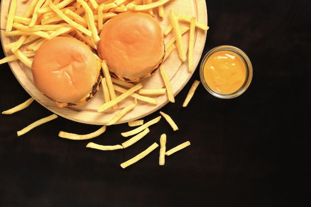 Cheeseburgers et frites sur une planche à découper vue de dessus fond en bois foncé Restauration rapide