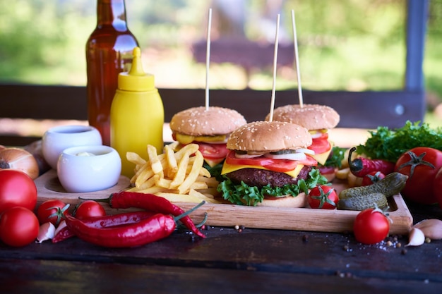 Cheeseburgers servis avec frites et légumes sur une table en bois sur une table de pique-nique à l'extérieur