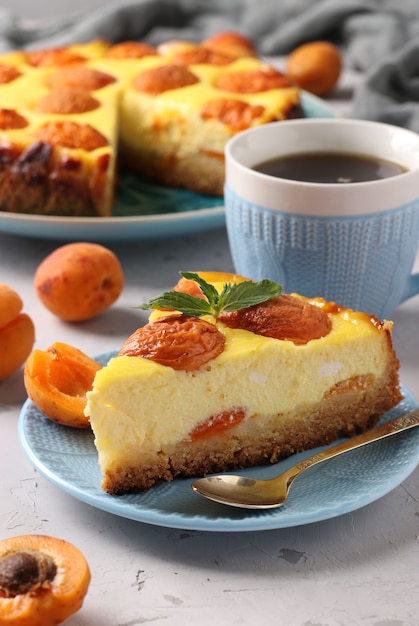Cheesecake aux abricots avec un morceau découpé, situé sur une plaque bleue et une tasse de café, format vertical, gros plan